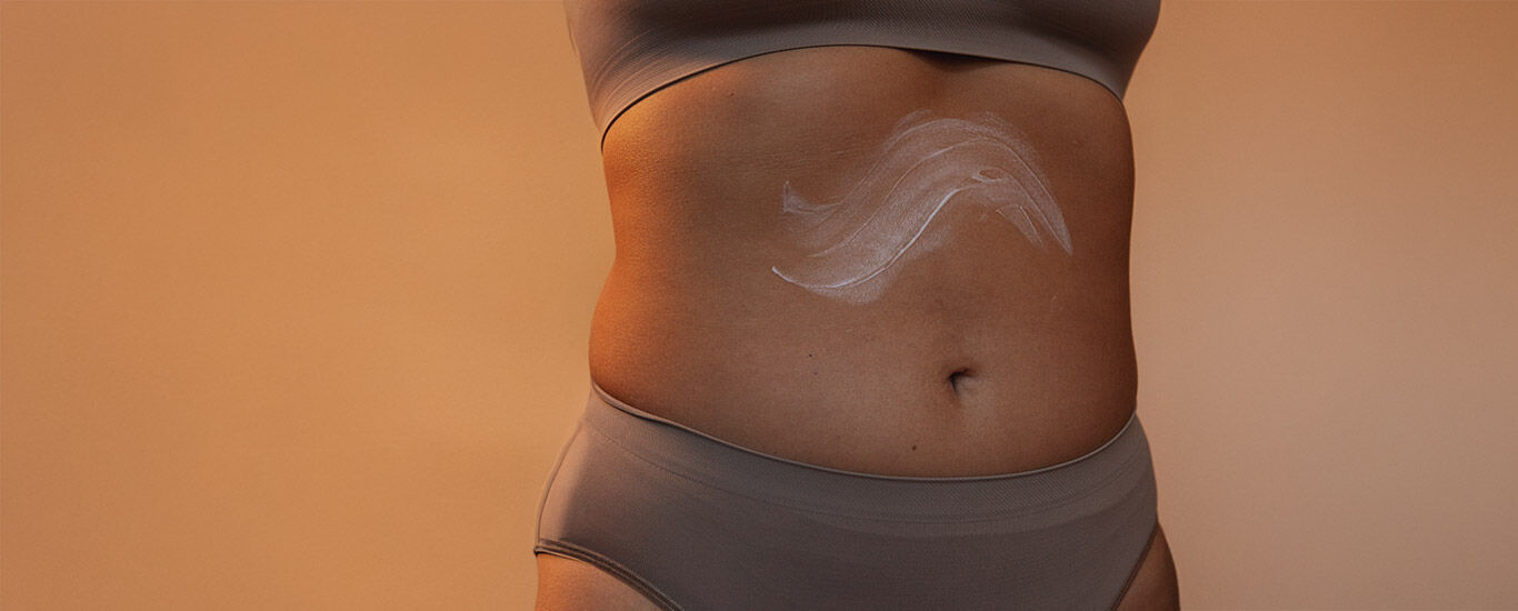 Close-up van de buik van een vrouw met cr&egrave;me erop.